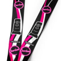 Detalle del diseño del lanyard Cocoloco con logotipos, moáis y colores negro, rosa y blanco.